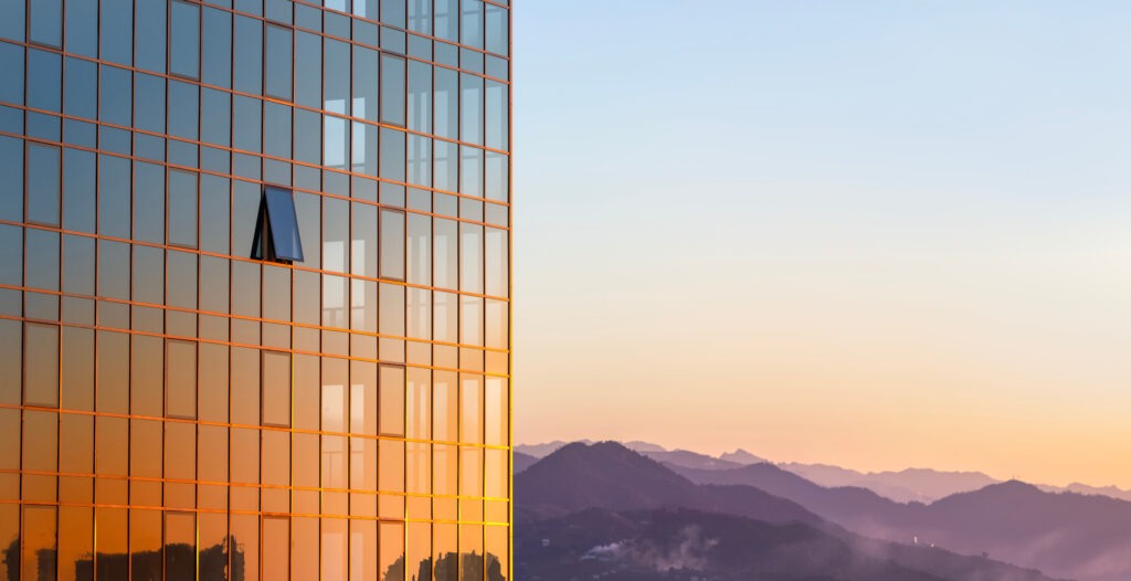 The glass wall of a modern building against the background of the sky and mountains in the rays of a golden sunset